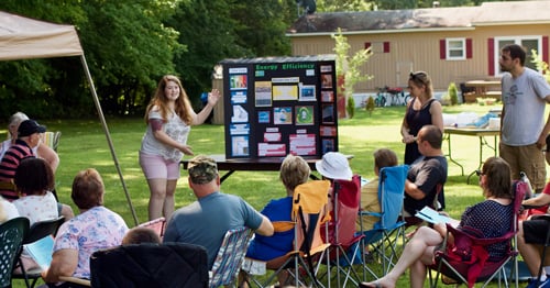 Mascoma Meadows residents sit in folding chairs outdoors and learn about the solar project.